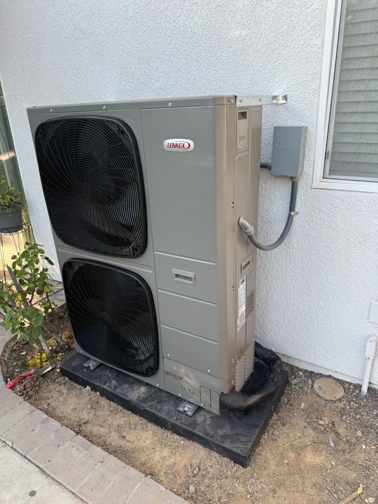 Exterior air conditioning unit installed next to a house, featuring dual fans and electrical connections.